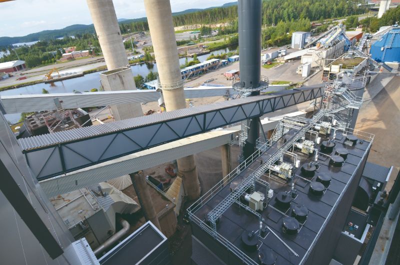 Näkymä voimalaitoksen katolta: putkisilta, savupiiput ja järvimaisema.